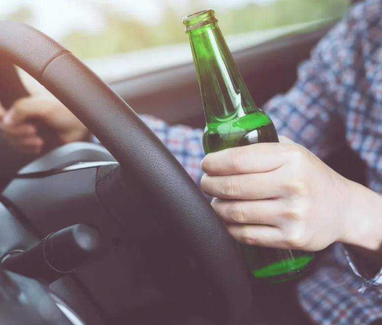Driver holding an open bottle behind the steering wheel